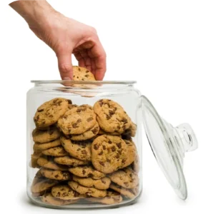 A person is reaching for cookies in a glass jar.