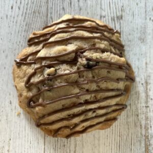 Cookie with chocolate drizzle on wooden surface.