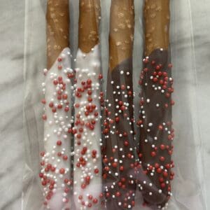 Three chocolate-covered pretzel sticks with white and red sprinkles in plastic wrapping.
